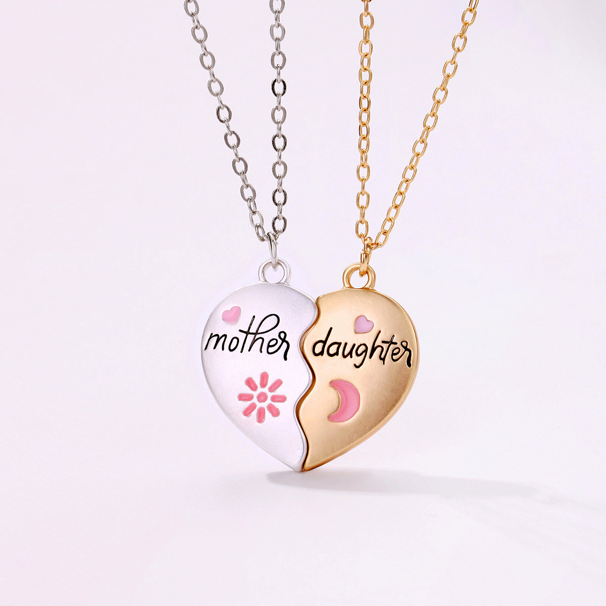 A two-piece heart-shaped necklace set with "Mother" on a silver pendant and "Daughter" on a gold pendant, featuring pink heart and moon details - front view