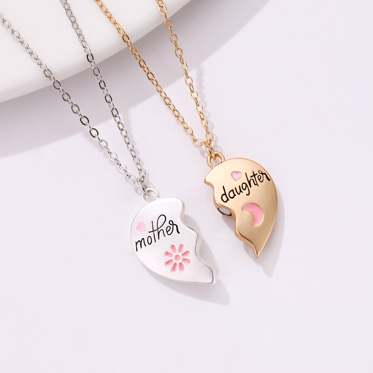 A two-piece heart-shaped necklace set with "Mother" on a silver pendant and "Daughter" on a gold pendant, featuring pink heart and moon details - separate pendants before attaching