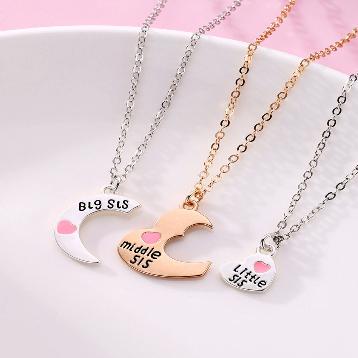A 3-piece sister necklace set featuring interlocking heart-shaped pendants labeled "Big Sis," "Middle Sis," and "Little Sis" with silver and gold chains. - separate necklaces on a plate view