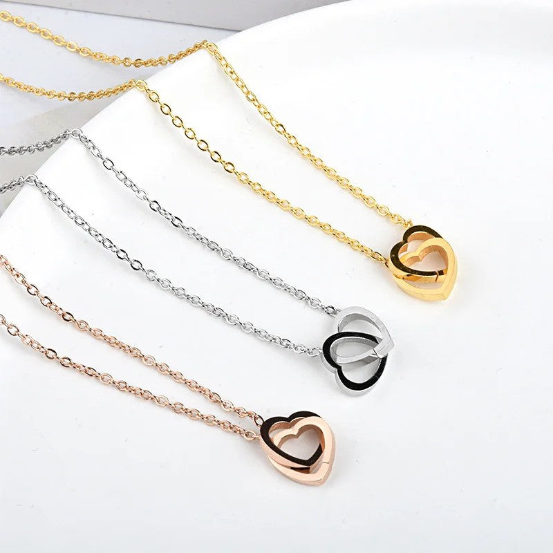 Solo Love Interlocking Hearts Necklaces in three colors—rose gold, silver, and gold—displayed side by side on a table.