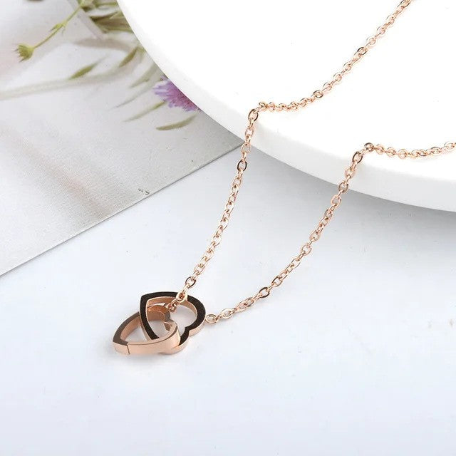 Solo Love Interlocking Hearts Necklace in rose gold stainless steel, featuring two elegant interlocking heart pendants displayed on a table