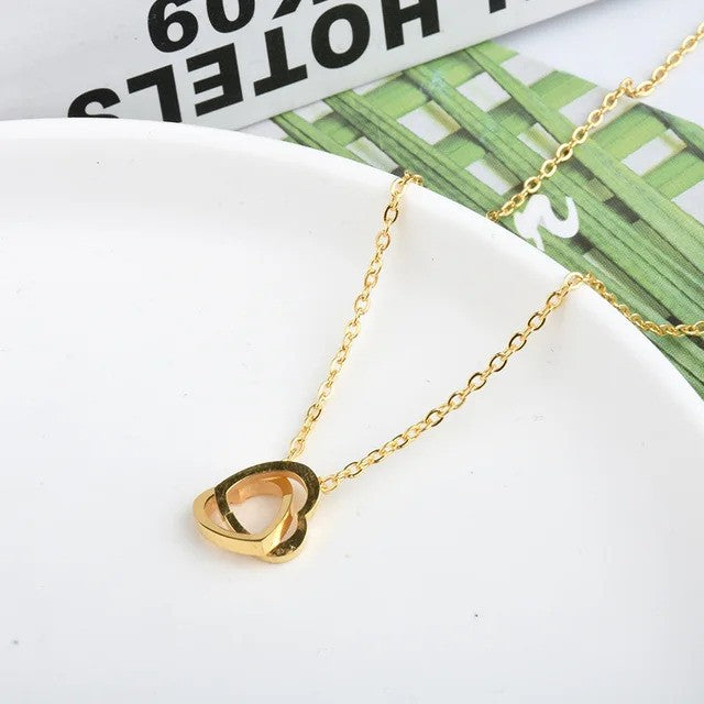 Solo Love Interlocking Hearts Necklace in gold stainless steel, featuring two elegant interlocking heart pendants displayed on a table