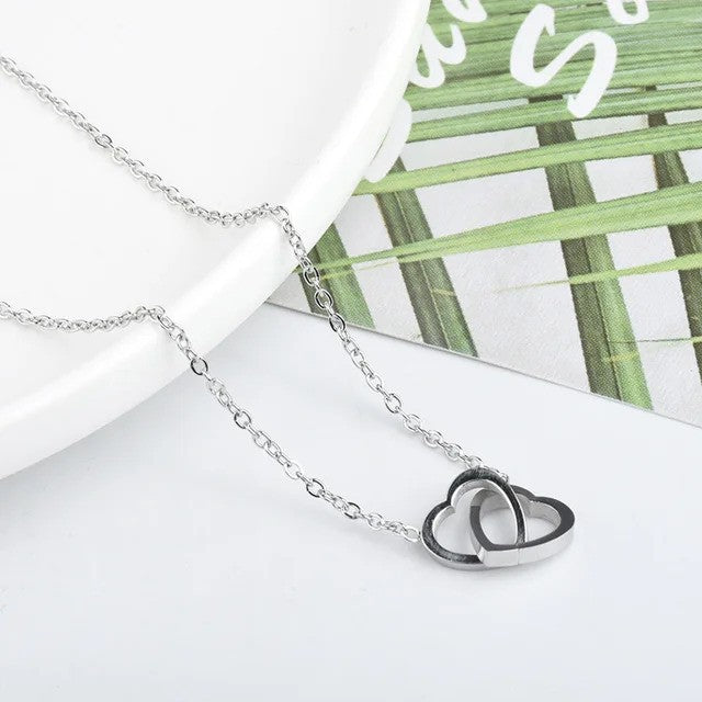 Solo Love Interlocking Hearts Necklace in silver stainless steel, featuring two elegant interlocking heart pendants displayed on a table
