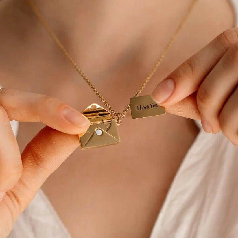 A person holding a gold Custom Engraved Love Letter Necklace, revealing an open envelope pendant with a hidden engraved message that reads "I Love You."