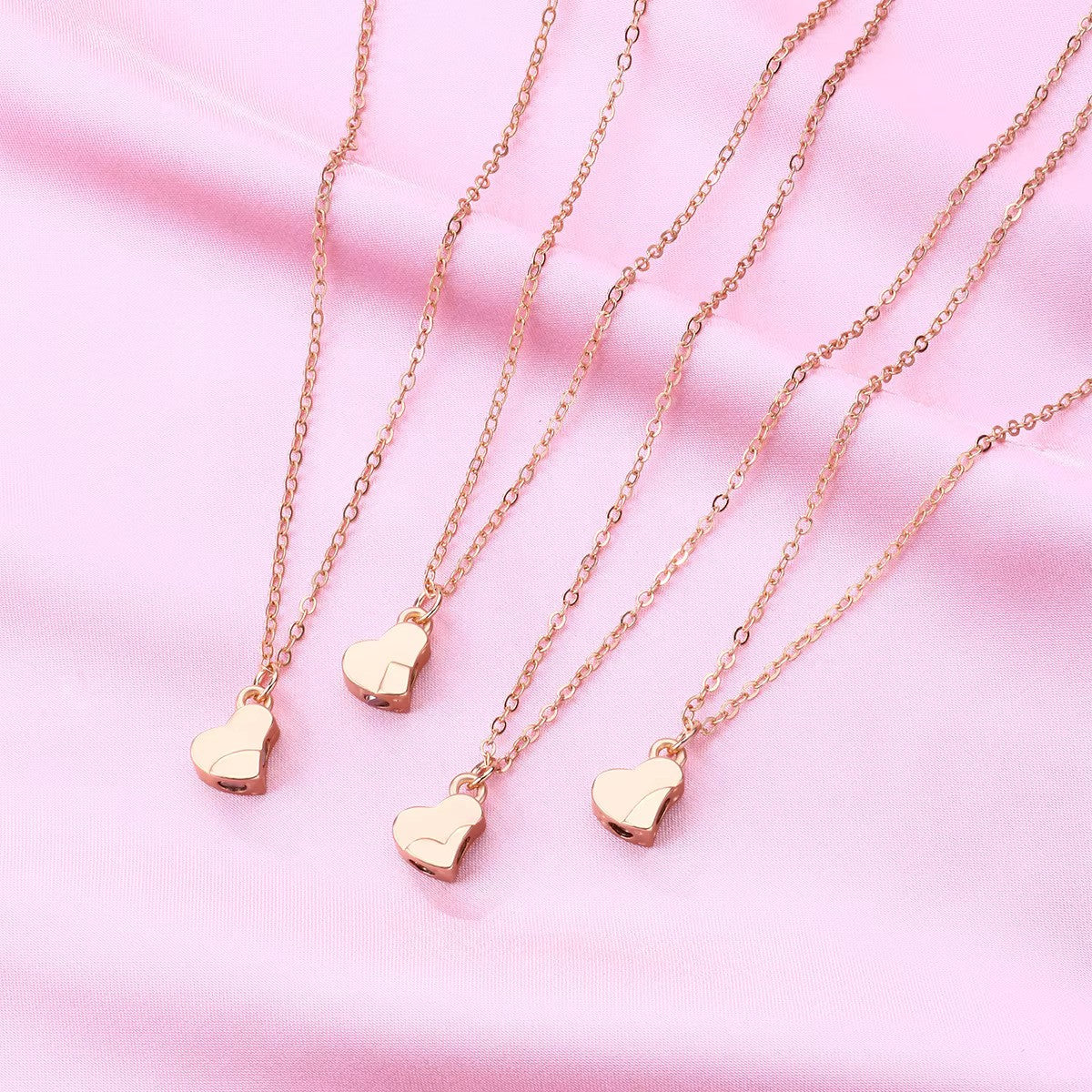 Gold Four-Leaf Clover Heart Magnetic Necklace displayed as 4 separate necklaces before being attached, laid on soft pink fabric. Each pendant features an interlocking heart design, symbolizing connection and love.