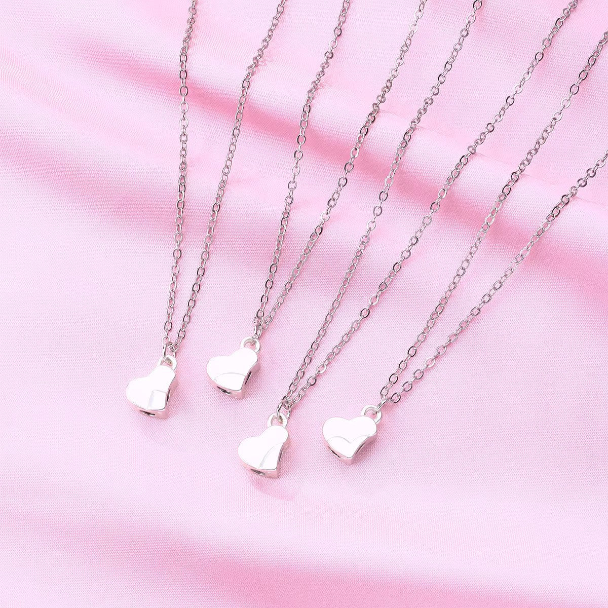 Silver Four-Leaf Clover Heart Magnetic Necklace displayed as 4 separate necklaces before being attached, laid on soft pink fabric. Each pendant features an interlocking heart design, symbolizing connection and love.