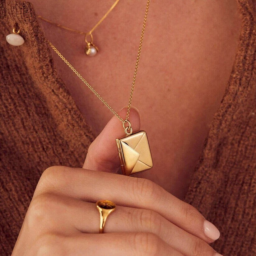 A person wearing and holding a gold Custom Engraved Love Letter Necklace close up.