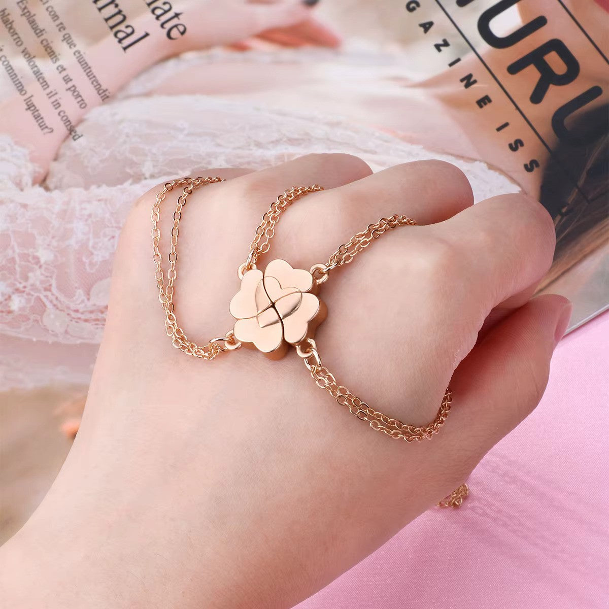 Gold Four-Leaf Clover Heart Magnetic Necklace set held in a clenched fist, with the necklaces displayed on top of the hand. The interlocking heart design symbolizes connection and love.
