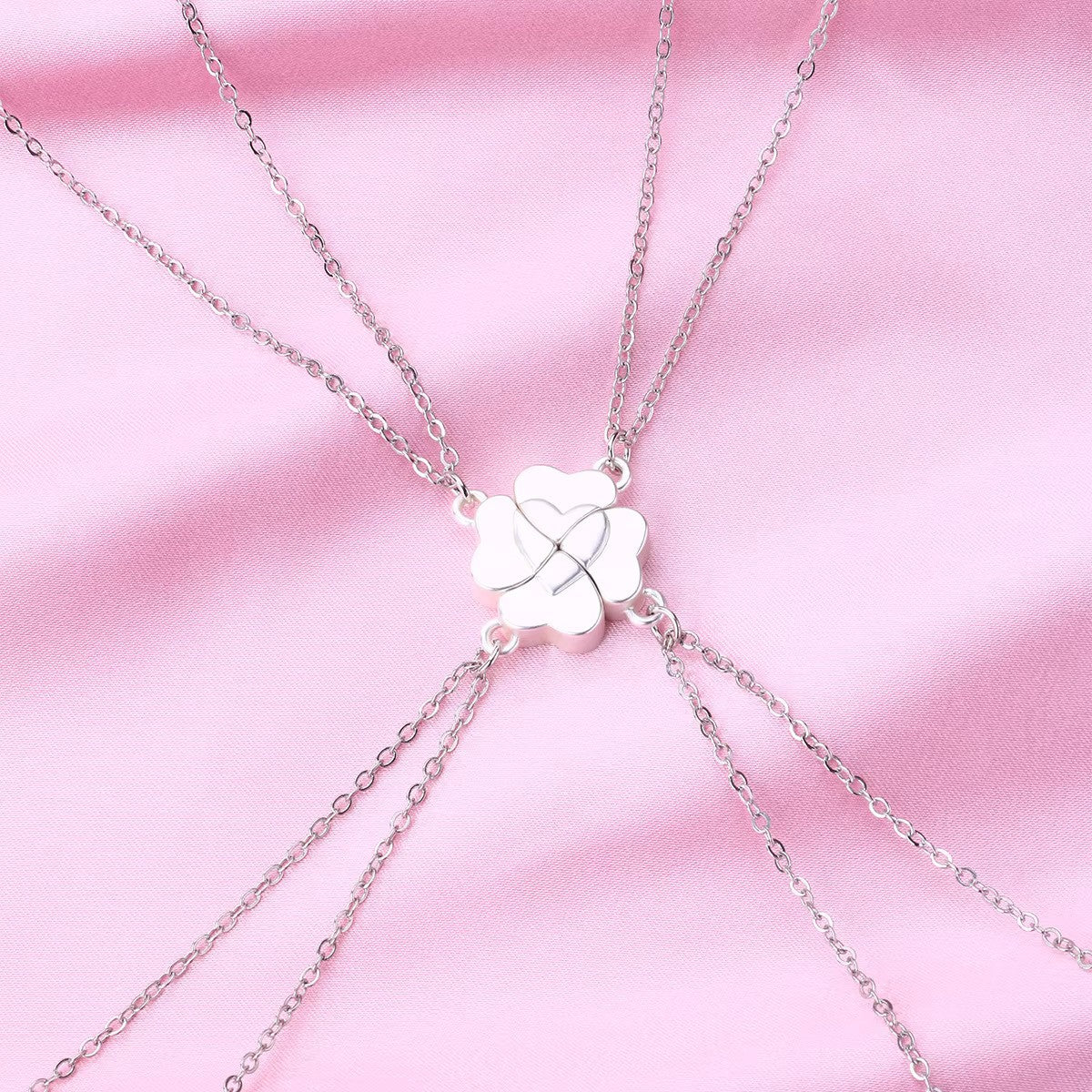 A silver Four-Leaf Clover Heart Magnetic Necklace displayed on soft pink fabric. The pendant features an interlocking heart design, symbolizing connection and love, with delicate gold chains extending from each side.